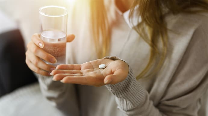 Close-up of a hand holding a single pill with a glass of water