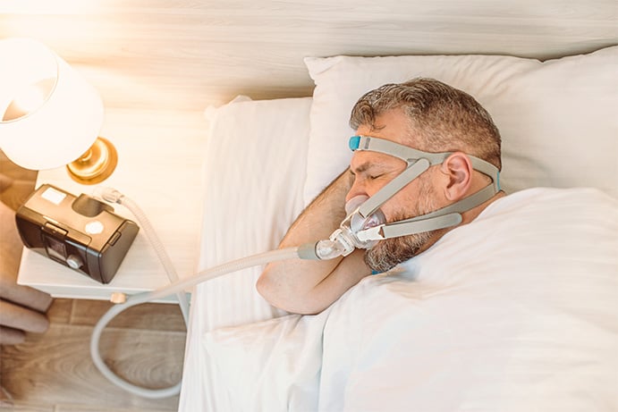 A sleeping man with chronic breathing issues utilizes a CPAP machine in bed.