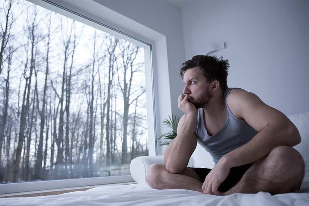 A depressed man sitting on a bed, lost in thought.